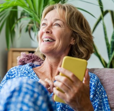 Beautiful mature senior woman at home, domestic life and leisure moments - 50-60 years old pretty female adult relaxing on the sofa and using smartphone